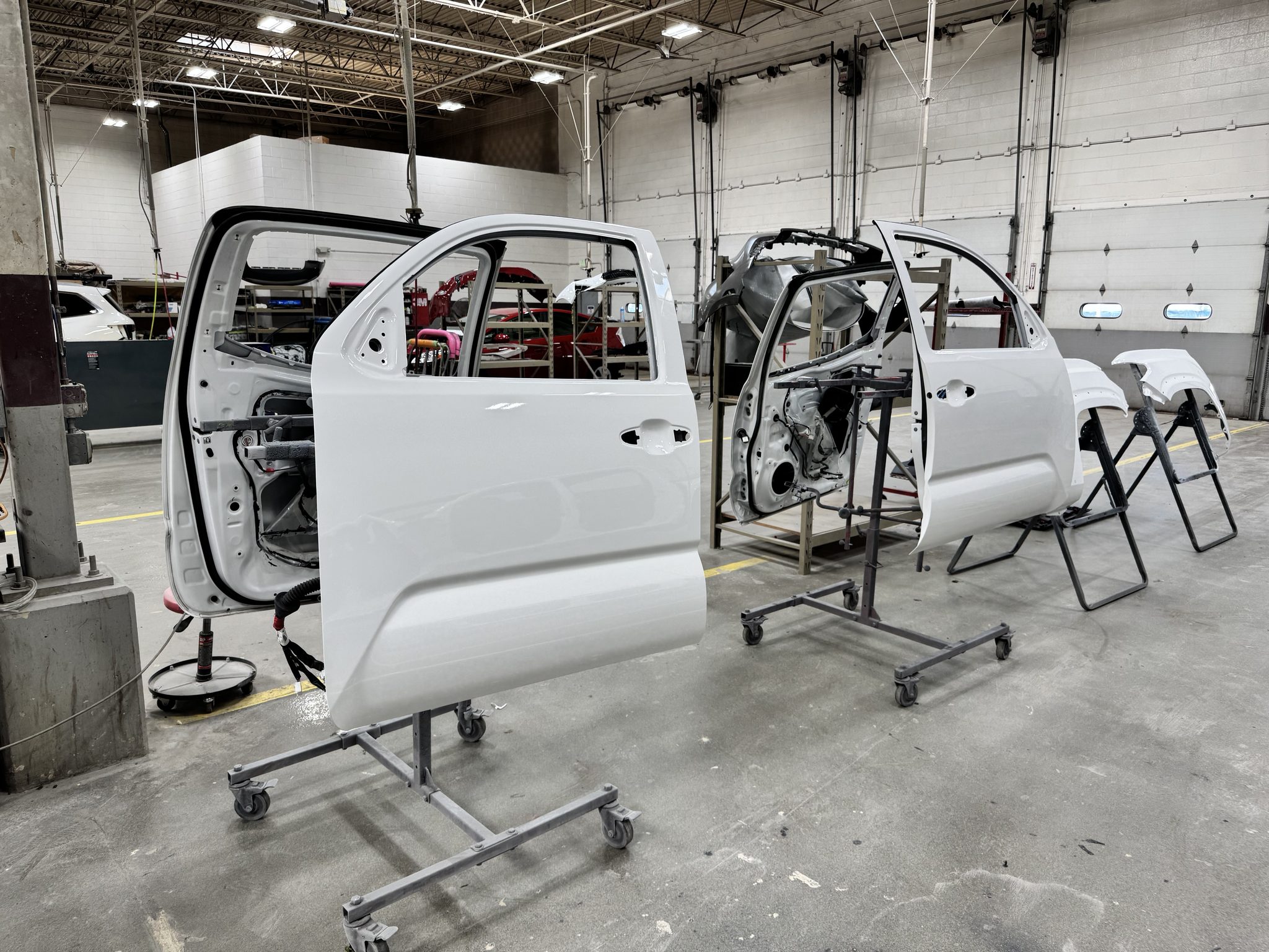 Freshly repainted Super White Toyota Tacoma doors on body stands waiting to be reinstalled after a paint warranty refinish at Bob Rohrman Collision Repair Center in Lafayette, Indiana