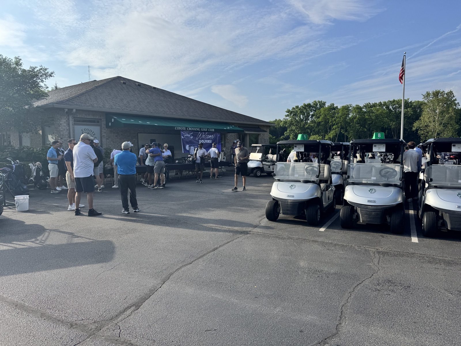 Golfers gathering at the Coyote Crossing Golf Club clubhouse for the Restored golf outing in West Lafayette, Indiana, with E-Z-GO carts lined up and a Welcome Golfers banner
